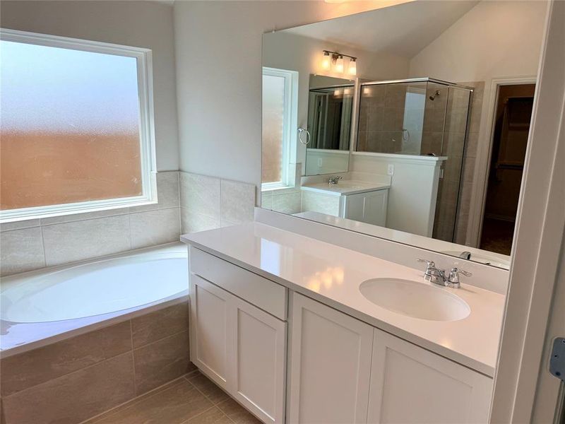 Bathroom featuring an undermount tub with tile surround, frosted window, dual white shaker vanities with integrated sinks, and a framed glass shower enclosure