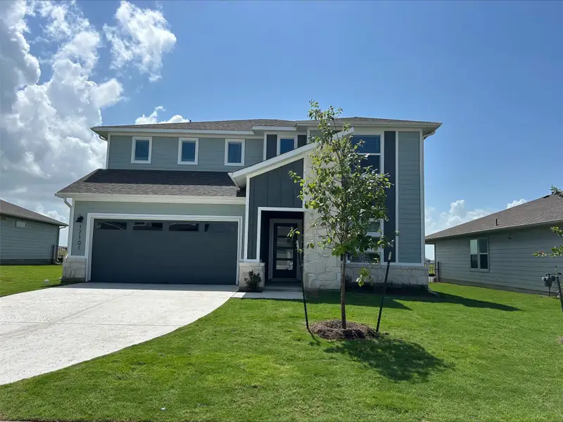 View of front of property featuring stone siding, concrete driveway, a garage, a front lawn, and board and batten siding View of front of property featuring stone siding, concrete driveway, a garage, a front lawn, and board and batten siding