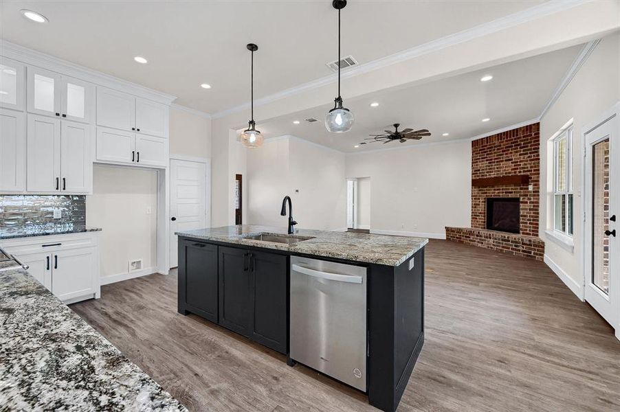 Kitchen featuring light hardwood / wood-style flooring, a brick fireplace, white cabinetry, dishwasher, and sink