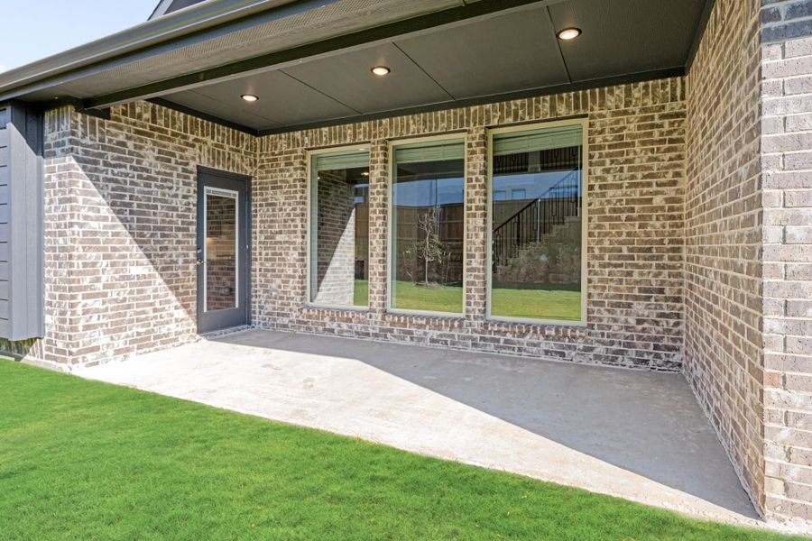 Covered back patio with brick exterior, recessed lighting, large windows, and concrete floor next to green lawn. Covered back patio with brick exterior, recessed lighting, large windows, and concrete floor next to green lawn.