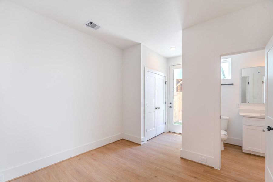 This bright room features light wood flooring, a closet with double doors, and access to a small bathroom with modern fixtures. A glass door opens to the outside, providing natural light and a view of the yard.Photo Disclaimer: Photos are representative of the community and may depict a similar floor plan, model home, or previously completed residence. This bright room features light wood flooring, a closet with double doors, and access to a small bathroom with modern fixtures. A glass door opens to the outside, providing natural light and a view of the yard.Photo Disclaimer: Photos are representative of the community and may depict a similar floor plan, model home, or previously completed residence.