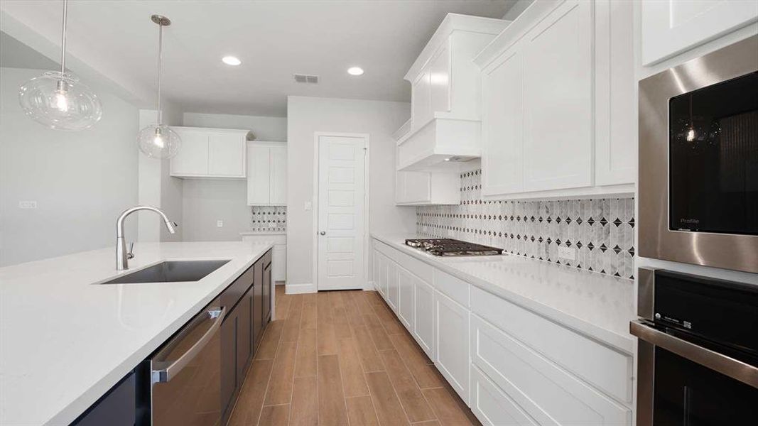 Kitchen featuring appliances with stainless steel finishes, sink, backsplash, decorative light fixtures, and white cabinets