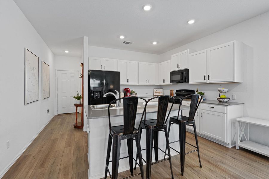 Kitchen with light wood-type flooring, black appliances, a kitchen breakfast bar, white cabinetry, and recessed lighting