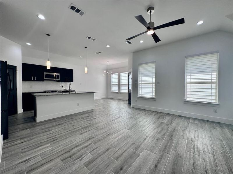 Living room with ceiling fan with notable chandelier, wood-type flooring, and sink