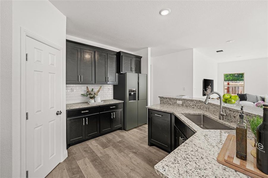 Kitchen with decorative backsplash, light stone counters, sink, light hardwood / wood-style flooring, and stainless steel fridge with ice dispenser