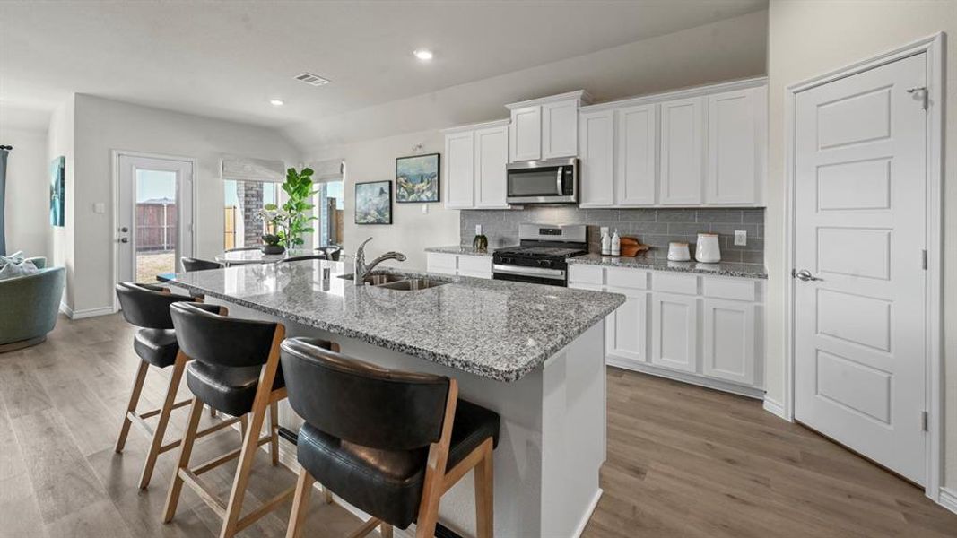 Kitchen with backsplash, white cabinets, light stone counters, a kitchen island with sink, and a breakfast bar