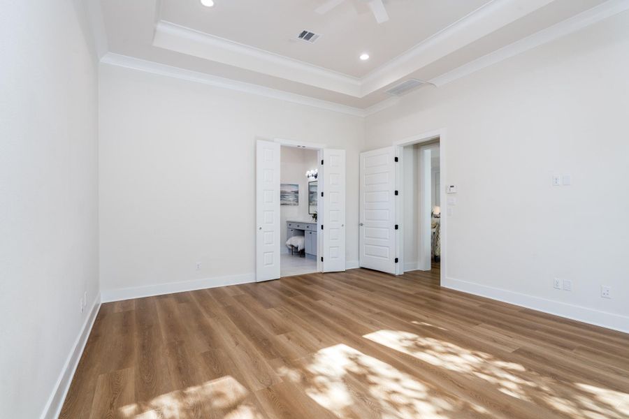 Primary bedroom with tray ceiling, recessed lighting, and warm vinyl flooring—features dual-door access to ensuite bath. Primary bedroom with tray ceiling, recessed lighting, and warm vinyl flooring—features dual-door access to ensuite bath.