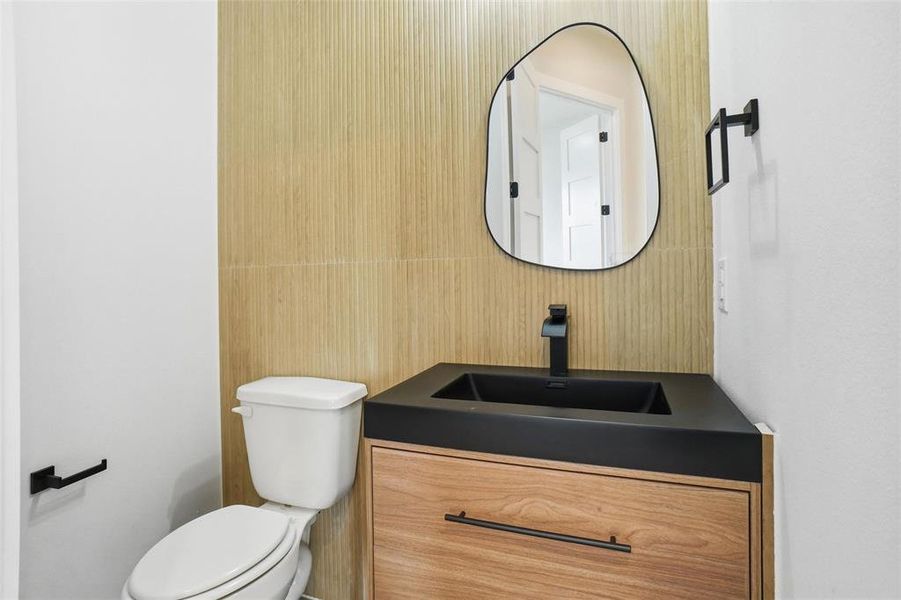 Stylish powder bath featuring a modern vanity with matte black fixtures and a wood accent wall.