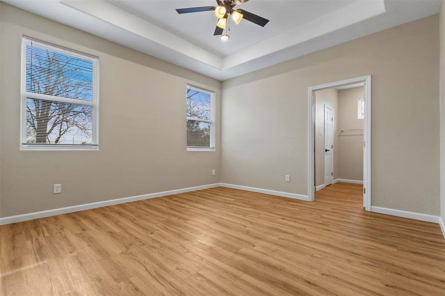 Spare room featuring a raised ceiling, light wood-style flooring, and a ceiling fan
