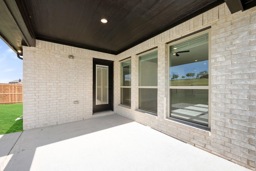 Covered back patio with concrete floor, light brick exterior, dark wood ceiling, and large windows beside back door.