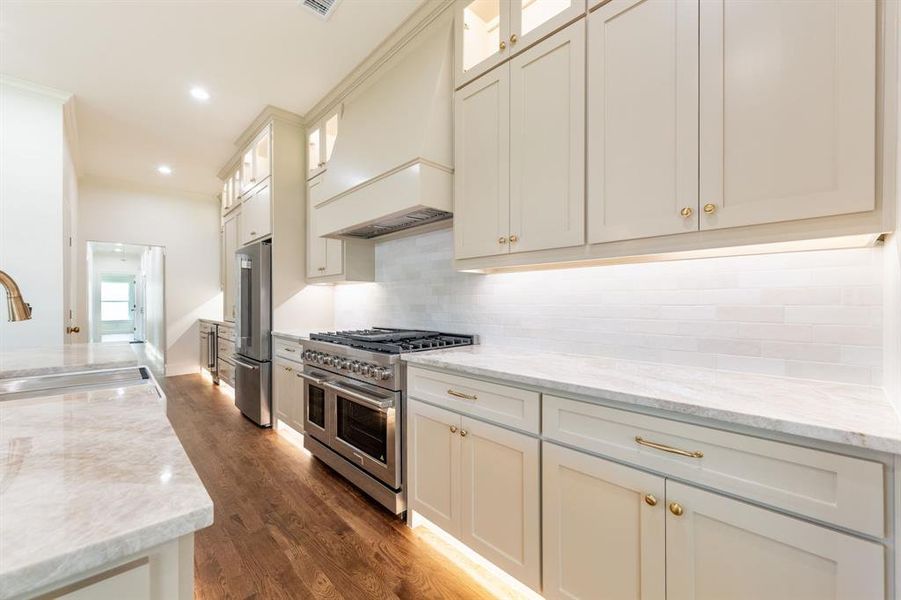 Gourmet kitchen featuring a stainless steel range, matching refrigerator, light-toned cabinetry, light stone countertops, and wood-finish flooring Gourmet kitchen featuring a stainless steel range, matching refrigerator, light-toned cabinetry, light stone countertops, and wood-finish flooring