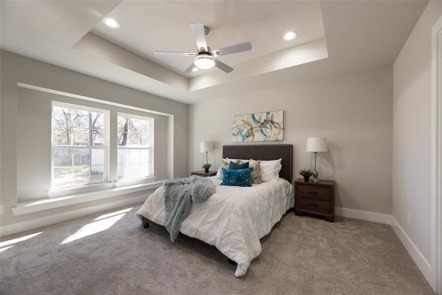 Carpeted bedroom with a raised ceiling and ceiling fan