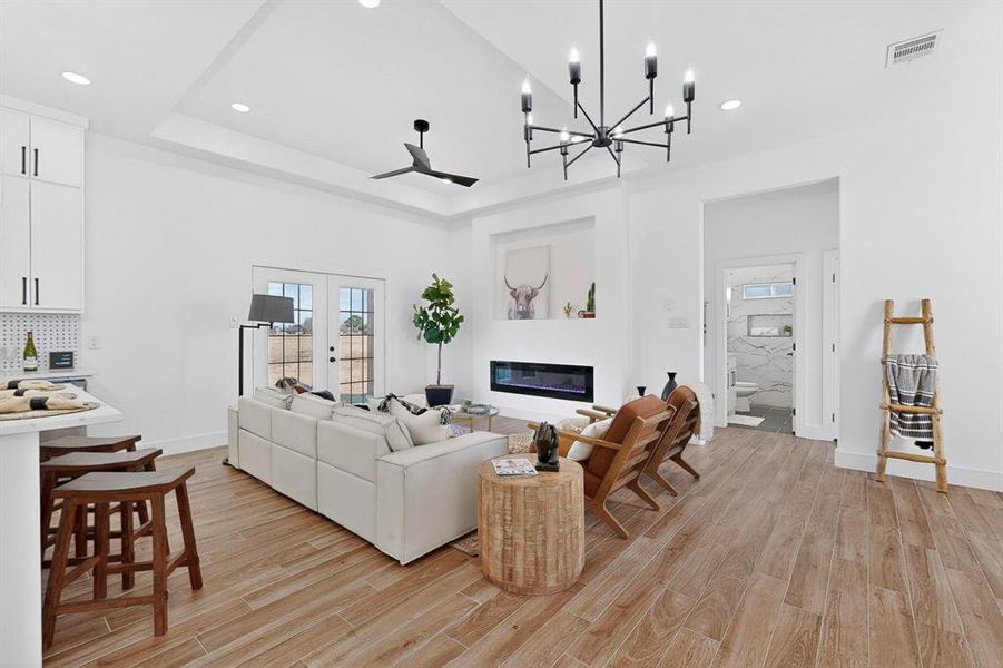 Living room with a chandelier, light wood-style floors, a glass covered fireplace, french doors, and recessed lighting