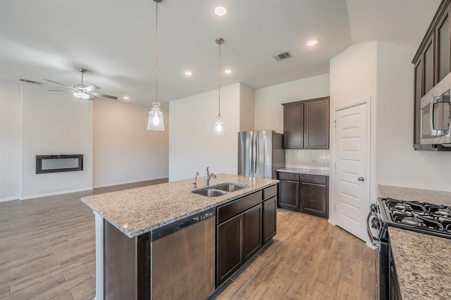 Kitchen featuring dark brown cabinets, decorative light fixtures, stainless steel appliances, light stone countertops, and recessed lighting Kitchen featuring dark brown cabinets, decorative light fixtures, stainless steel appliances, light stone countertops, and recessed lighting
