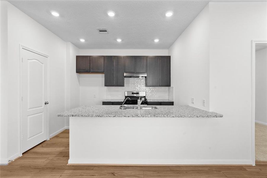 Additional view of this stunning kitchen! Featuring stained cabinets, granite countertops, modern backsplash, stainless steel appliances, recessed lighting, and custom paint.