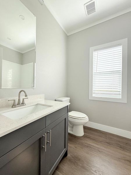 A well-lit bathroom featuring a modern vanity with a single sink and warm-toned flooring. Bathroom 3
