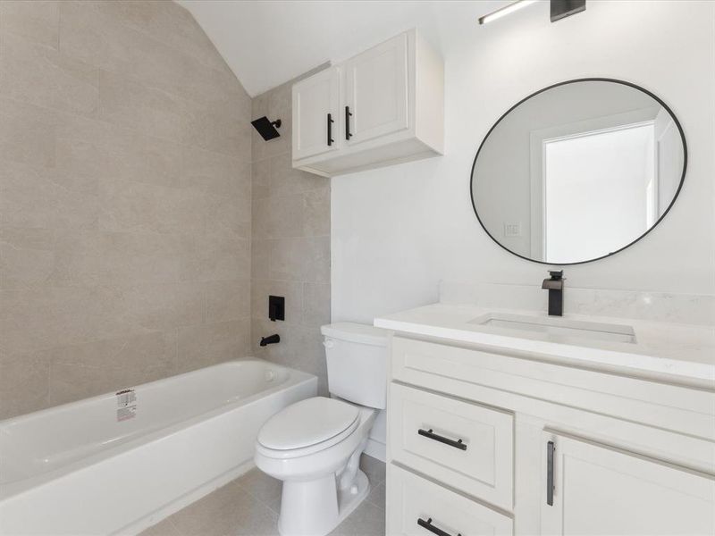 Full bath with lofted ceiling, toilet, tile patterned floors,  shower combination, and vanity