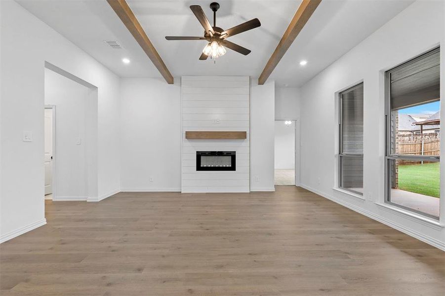 Unfurnished living room featuring a large fireplace, beamed ceiling, light hardwood / wood-style flooring, and ceiling fan