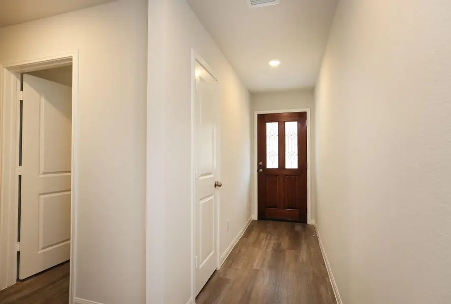 The bright, narrow hallway Entry with light-colored walls and vinyl plank flooring includes two doors on the left side, providing additional access to bedrooms, the Utility Room, and Garage.