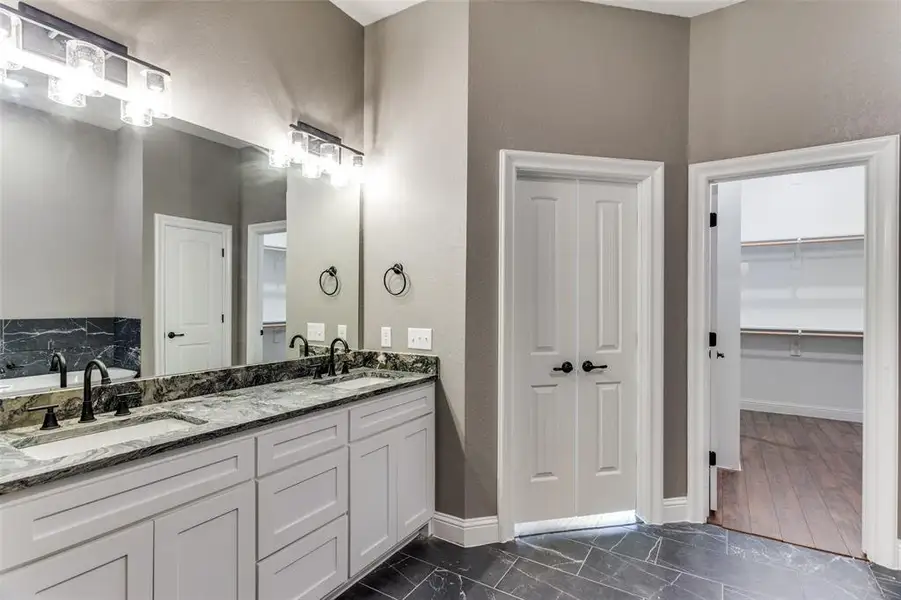Full bathroom with double vanity, a textured wall, and a spacious closet Full bathroom with double vanity, a textured wall, and a spacious closet