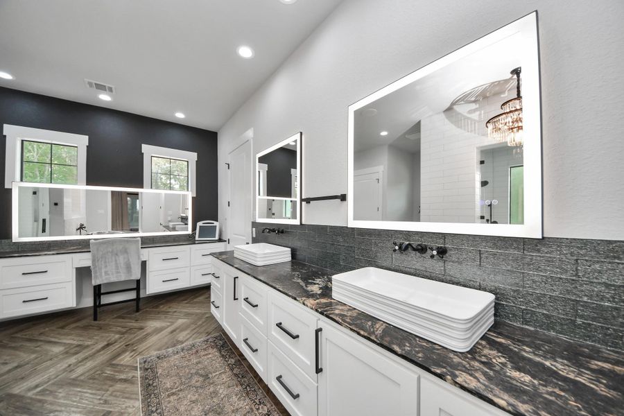 Luxurious bathroom featuring sleek double vanities with illuminated mirrors, elegant tile backsplash, and stylish herringbone flooring.
