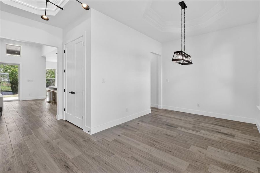 Unfurnished dining area featuring a raised ceiling, wood finished floors, and crown molding