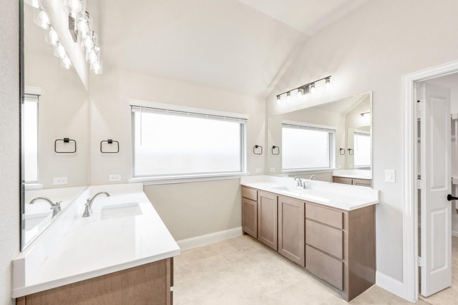 Bathroom with dual vanities, brown cabinets, white countertops, and vaulted ceiling