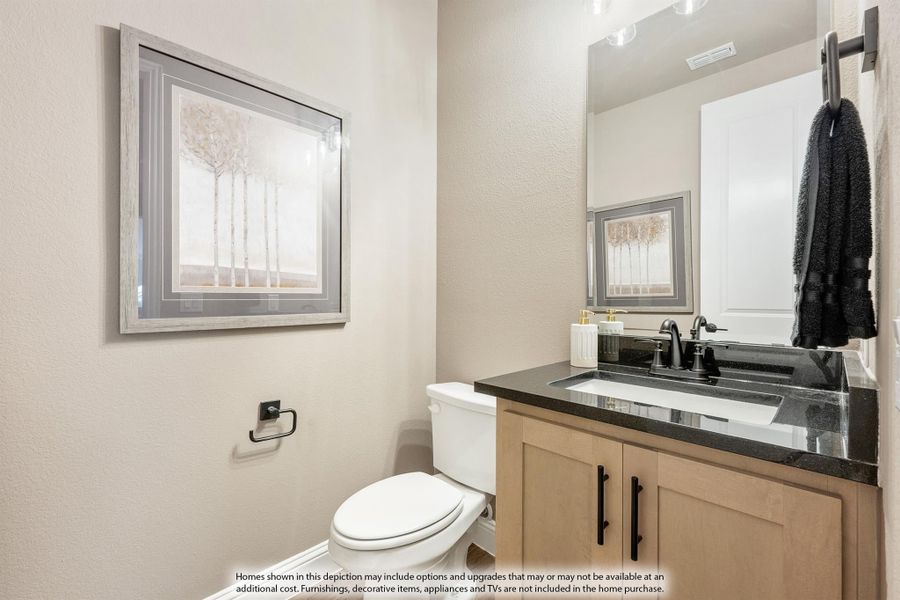 Half bathroom with wood vanity, dark countertop, white toilet, and large mirror Half bathroom with wood vanity, dark countertop, white toilet, and large mirror