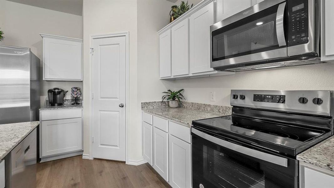 The kitchen features white cabinetry, granite countertops, and stainless steel appliances including a microwave, electric range, and refrigerator