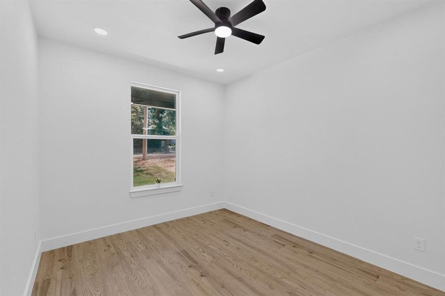 Bright room with wood-finish flooring, crisp white walls, and a ceiling fan with integrated lighting