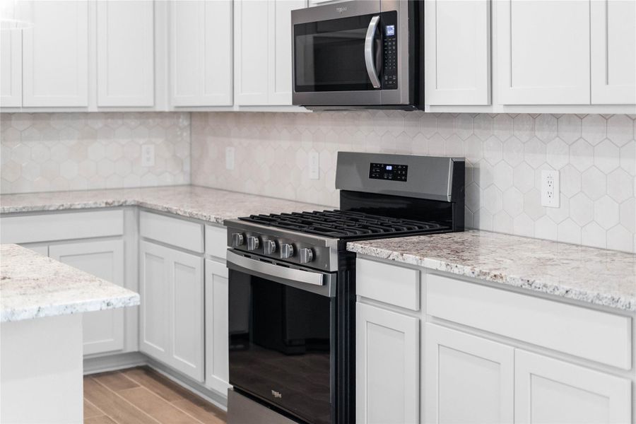 Showcased here is a Whirlpool gas range with center oval burner, paired with a steam microwave equipped with sensor cooking—all framed by an elegant tile backsplash.