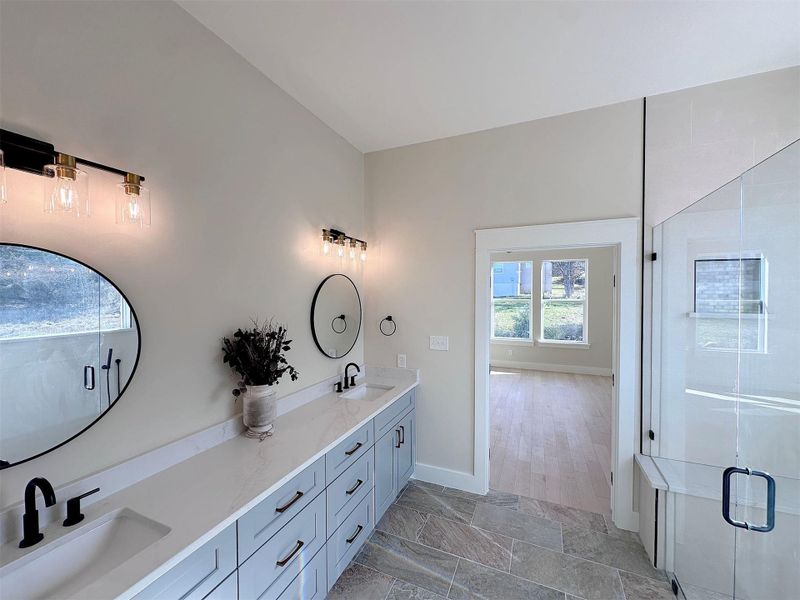 Full bath with a large walk-in shower w/seating bench & rimless glass enclosure, double vanity offering excellent storage drawer space, and easy care stone tile flooring