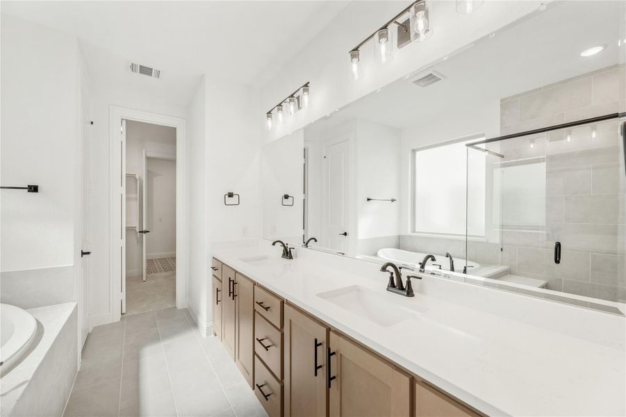 Master bathroom with double vanity, white countertops, glass shower, and soaking tub on tile floors