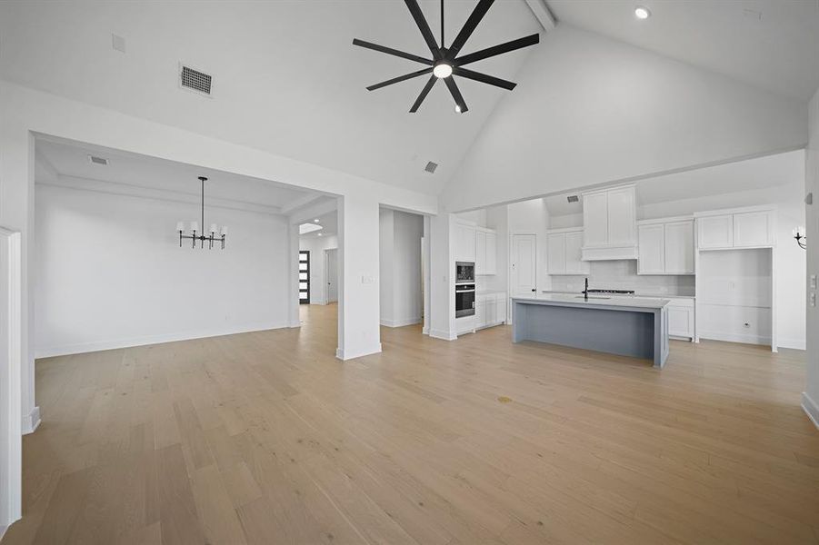 Unfurnished living room with a ceiling fan, high vaulted ceiling, beamed ceiling, light wood-style floors, and a chandelier