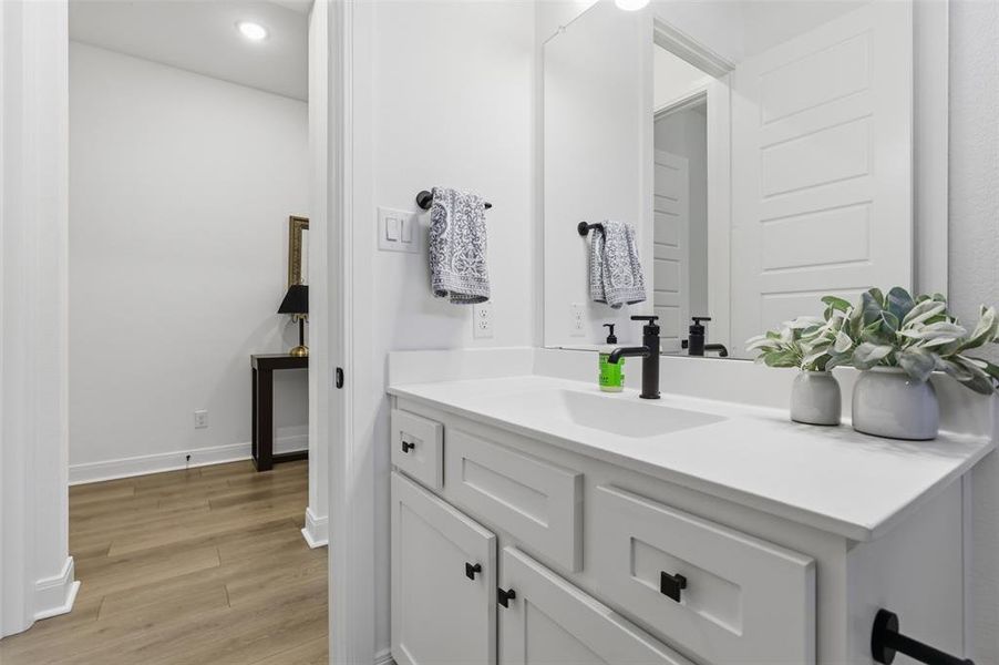 Bathroom vanity featuring white cabinetry with black hardware, a solid surface countertop, an undermount sink, and a matte black faucet Bathroom vanity featuring white cabinetry with black hardware, a solid surface countertop, an undermount sink, and a matte black faucet