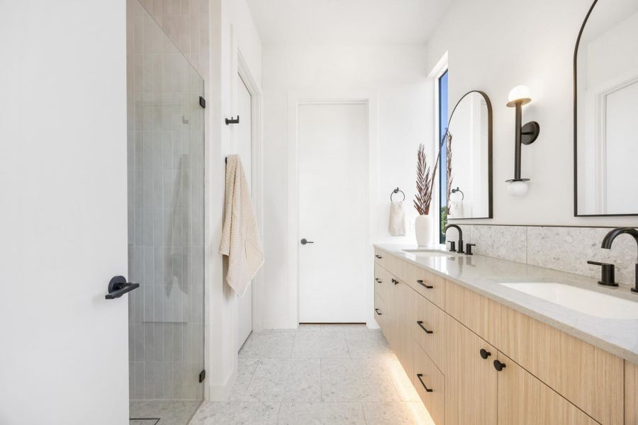 Bright bathroom featuring a dual vanity with light wood-finish cabinetry, under-cabinet lighting, and stone countertops