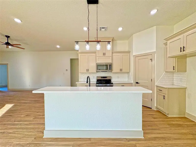 Kitchen with a center island with sink, pendant lighting, a textured ceiling, decorative backsplash, and stainless steel appliances