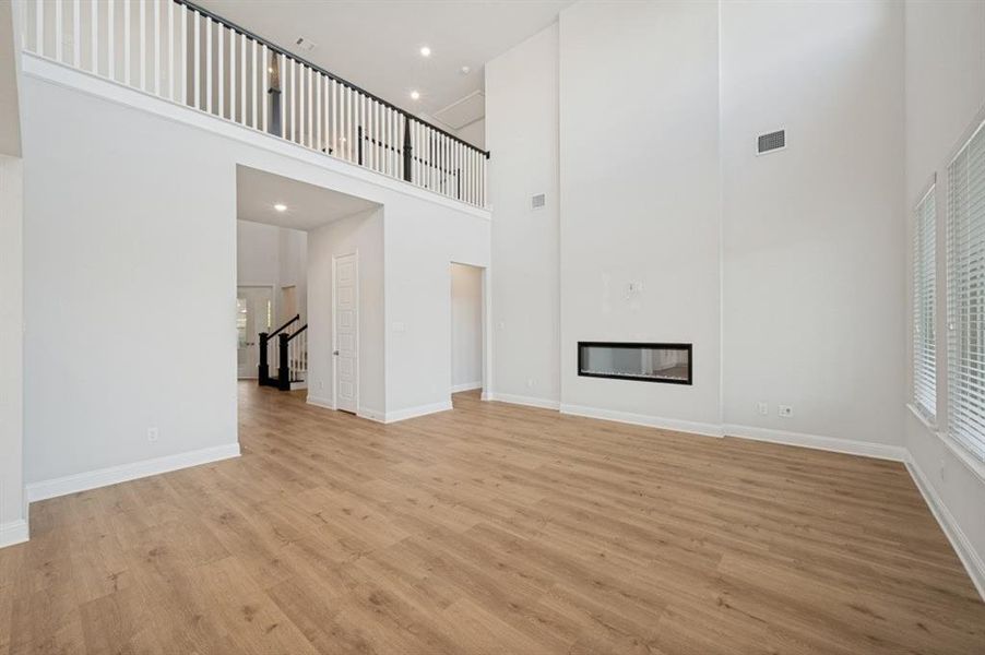 Spacious interior featuring high ceilings, wood-finish flooring, a contemporary linear fireplace, and multiple windows with blinds