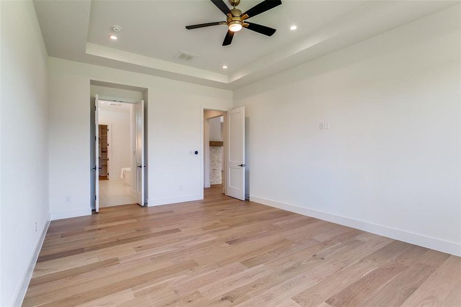 Unfurnished bedroom with light wood finished floors, ceiling fan, recessed lighting, and a tray ceiling