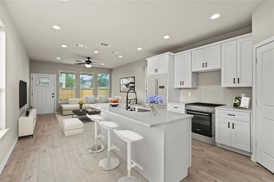 Kitchen with sink, a center island with sink, stainless steel range oven, white cabinetry, and built in fridge