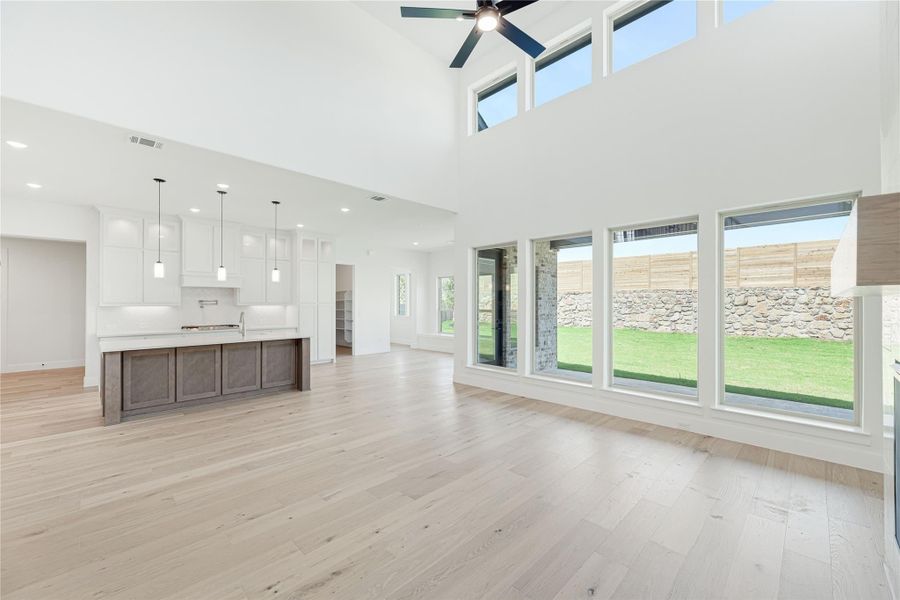 Open-concept living area with high ceilings, hardwood floors, and kitchen island with white cabinets and large windows
