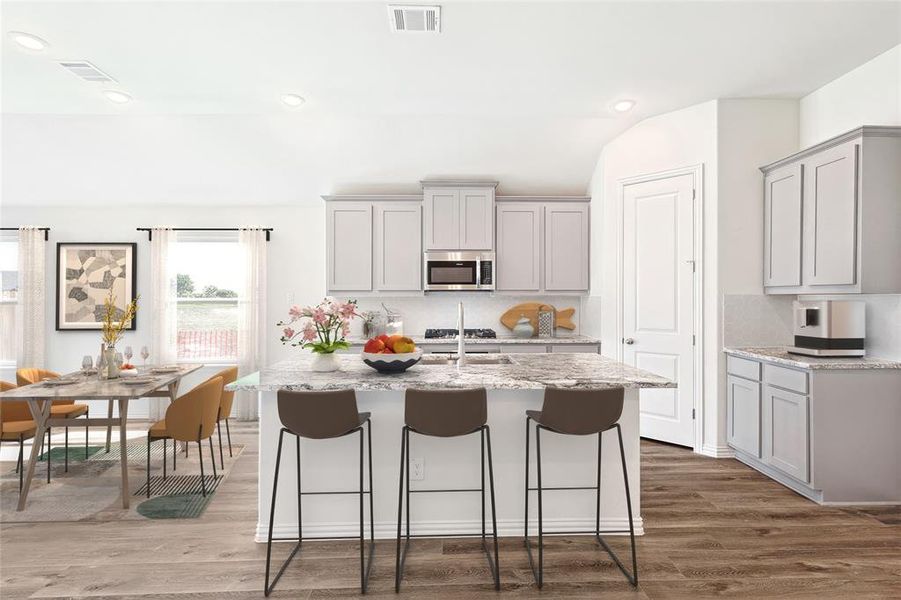 Kitchen with an island with sink, light stone countertops, wood-type flooring, vaulted ceiling, and gray cabinets