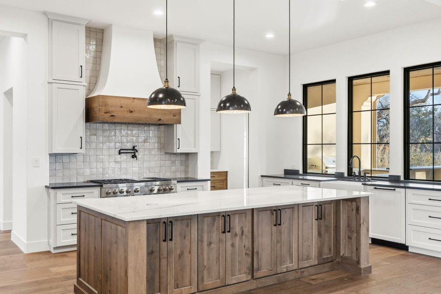 Two tone kitchen with dark wood finished floors, two tone color scheme, a center island, dark stone countertops, and decorative light fixtures