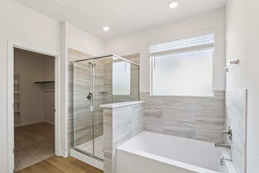 Full bath with a garden tub, light wood-style floors, a shower stall, a spacious closet, and recessed lighting Full bath with a garden tub, light wood-style floors, a shower stall, a spacious closet, and recessed lighting