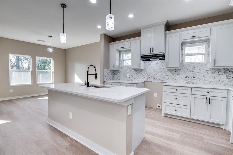 Kitchen featuring a wealth of natural light, a sink, light stone counters, under cabinet range hood, and decorative backsplash