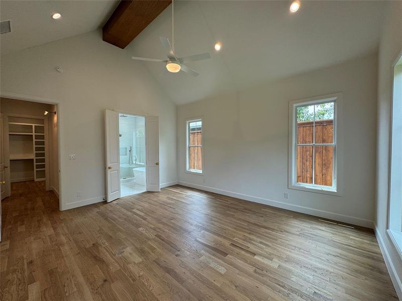 Unfurnished bedroom with a spacious closet, wood-type flooring, ceiling fan, high vaulted ceiling, and beamed ceiling