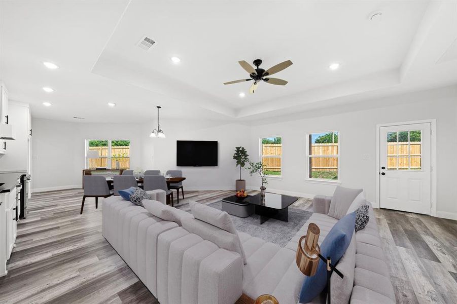 Living room with a raised ceiling, recessed lighting, light wood-style flooring, a chandelier, and a ceiling fan Living room with a raised ceiling, recessed lighting, light wood-style flooring, a chandelier, and a ceiling fan