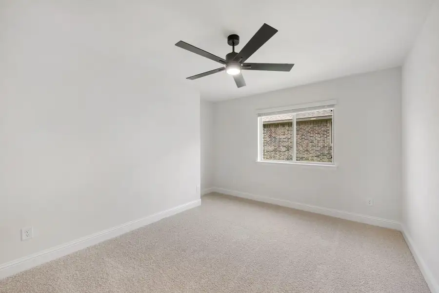 Empty bedroom with beige carpet, white walls, ceiling fan with light, and single window