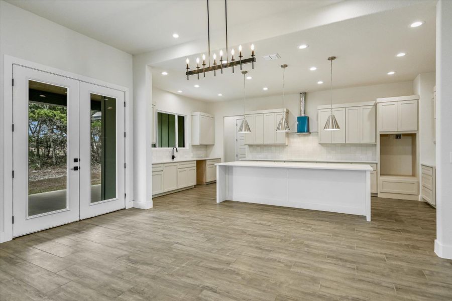 Kitchen featuring white cabinetry, french doors, decorative backsplash, and a large island