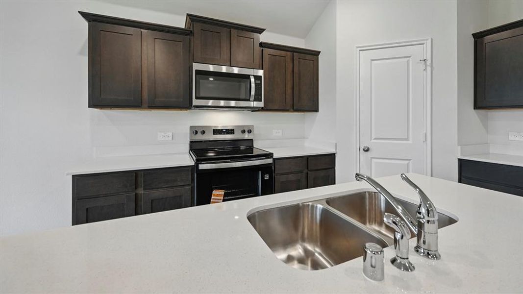 Kitchen featuring stainless steel appliances, dark brown cabinetry, and light stone countertops